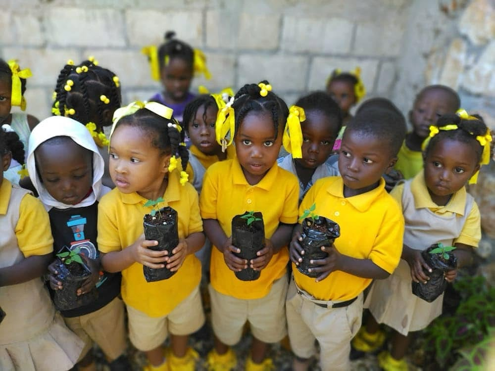 Children in golden-yellow uniforms holding seedling starts at a HavServe program in Haiti