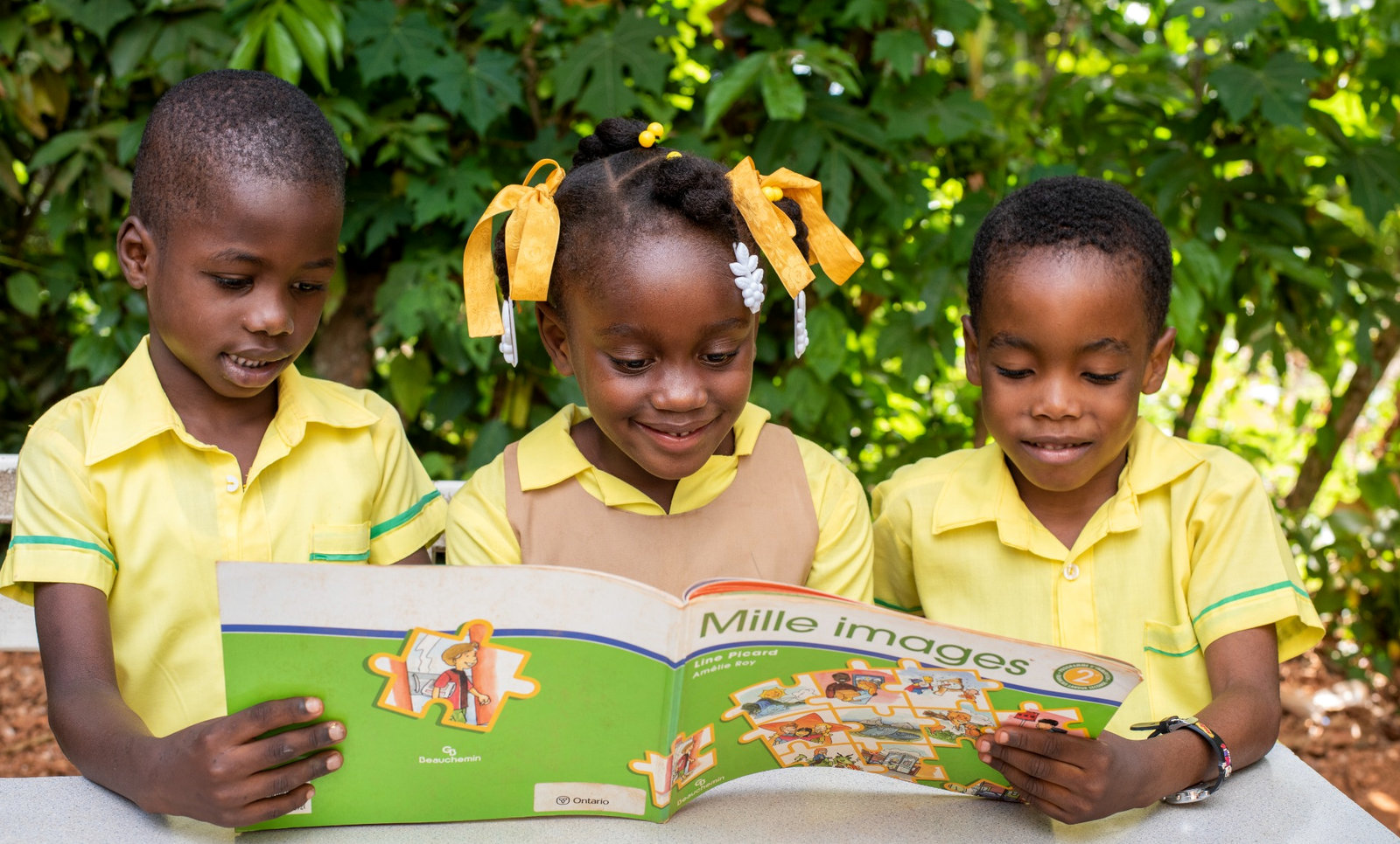 Students in yellow shirts read together outdoors at the Academy in Southern Haiti.